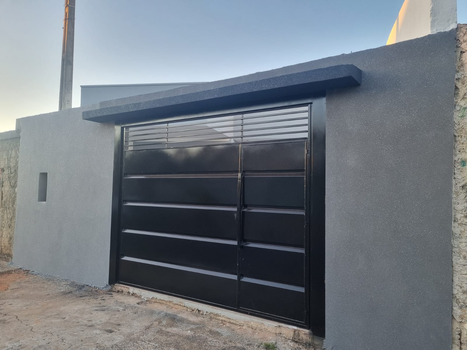Fachada cinza com portão metálico preto ao entardecer